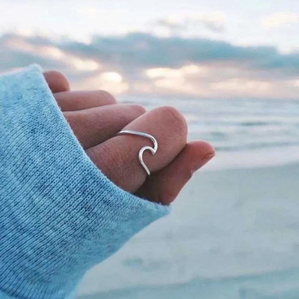 hand wearing a wave ring with the ocean behind in a cold day
