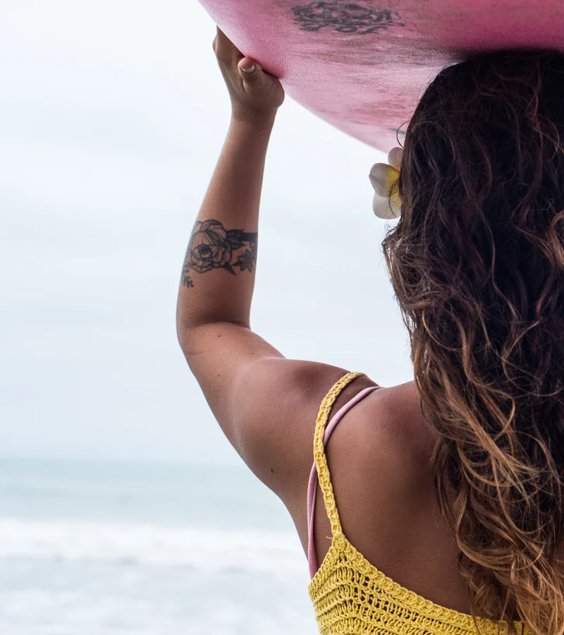 woman in yellow crop top carrying a surfboard