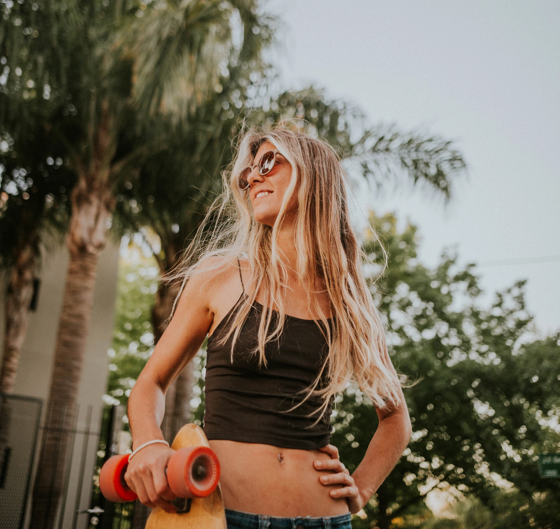 woman with sunglasses smiling and holding a longboard
