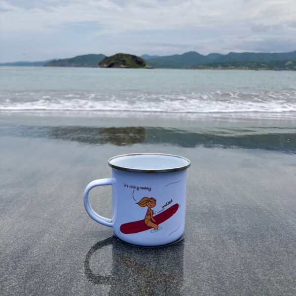 enamel surf mug with surfer girl illustration on a black sand beach and the ocean behind