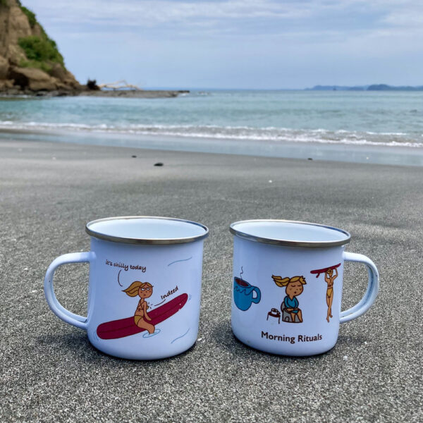 enamel surf mugs on the black sand of a beautiful beach with illustrations